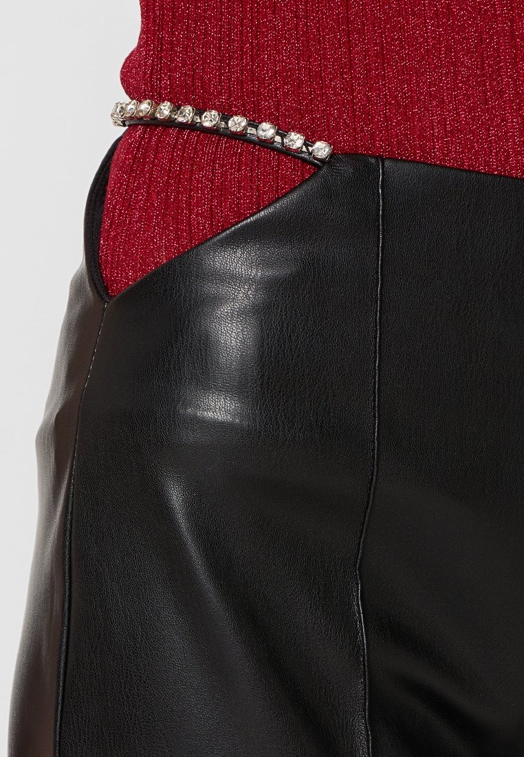 Zwarte leren broek met een gladde textuur, aangevuld met een zilveren gesp met studs. De bovenste stof is een textuur gebreide rode stof.