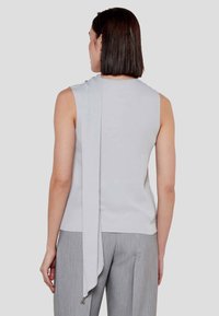 Top senza maniche grigio chiaro con dettaglio drappeggiato sul retro, realizzato in tessuto morbido; abbinato a pantaloni grigio chiaro con texture.