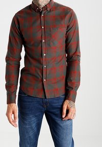 Męska koszula w kratę w kolorze zielonym i czerwonym, z kołnierzykiem na guziki, długimi rękawami, kieszenią na piersi i dopasowanym fasonem. Wykonana z miękkiego materiału.