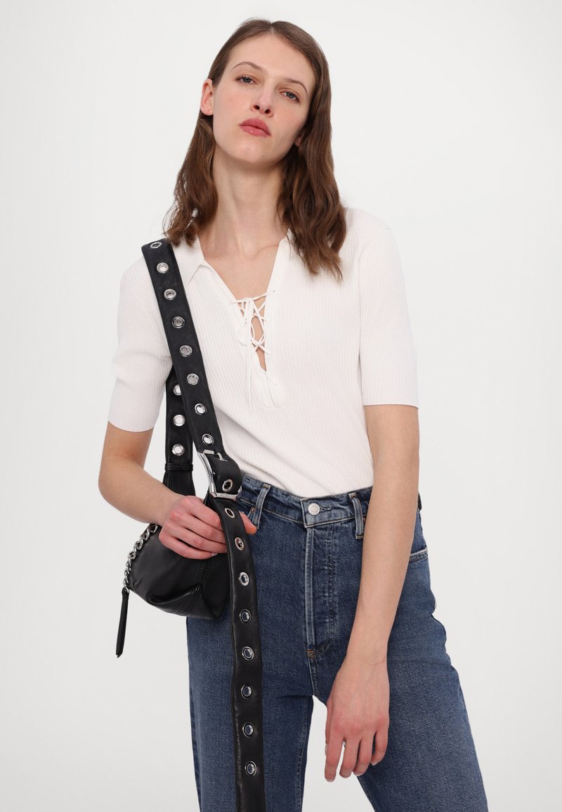 Haut blanc à côtes avec un détail de laçage, associé à un jean bleu taille haute et un sac noir avec une bandoulière cloutée.