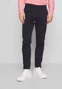 Czarne spodnie bawełniane o dopasowanym kroju, z zapięciem na guzik i szlufkami na pasek, zestawione z białymi tenisówkami, prezentujące gładką fakturę.