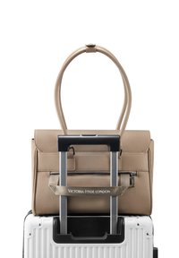 Borsa a tracolla in pelle beige con doppi manici, posizionata su una valigia bianca con ruote. Presenta una tasca con zip e un marchio sulla tracolla.