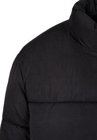 Chaqueta tipo puffer negra con cuello alto, textura acolchada y tejido suave. Compuesta de material ligero con un acabado mate.