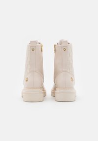 Botines beige con un panel trenzado, cuero suave, cremalleras laterales y una suela gruesa con acentos decorativos.
