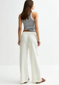 Witte wijde pantalons met een elastische tailleband, gemaakt van een lichtgewicht materiaal, gecombineerd met een gestreept tanktop. Bruine sandalen maken de outfit compleet.