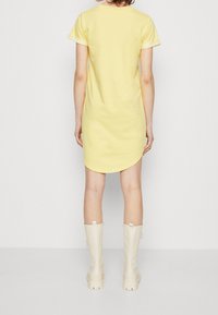 Robe jaune à manches courtes avec un ourlet arrondi, faite d'un tissu doux. Associée à des bottes beiges jusqu'aux genoux avec une semelle épaisse.