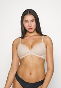 Sujetador de tela suave beige con tirantes delgados ajustables, escote en forma de V y copas moldeadas para un acabado sin costuras.