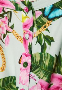 Bloemenschirt met roze bloemen, groene bladeren en blauwe vlindermotieven. Lichtgroene stof met knoopsluiting en kettingpatronen.