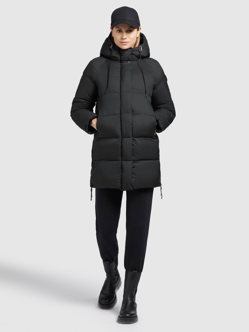 Doudoune noire avec capuche, dotée d'un design matelassé, de cordons de serrage et de poches latérales, associée à un pantalon noir et des bottines.