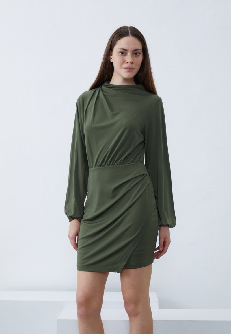 Olivengrünes Kleid mit langen Ärmeln, drapierter Gestaltung, gerafftem Taillenteil und einem seitlichen Schlitz. Glattes Material mit weicher Textur.