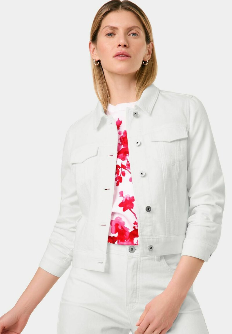 Weiße Denimjacke mit langen Ärmeln, Knopfschluss und zwei Brusttaschen. Darunter wird ein Oberteil mit floralem Muster und roten Akzenten getragen.