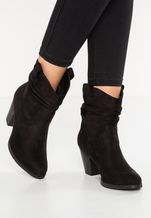 Botines de ante negros con un diseño relajado, puntera afilada y un tacón cuadrado texturizado. Detalles de costura visibles y un puño doblado.