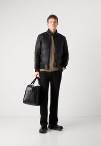 Melna vāka jaka ar ribotām piedurknēm virs olīvzaļas t-kreklā, apvienota ar melnām biksēm un strukturētu ādas somu. Apģērbu noslēdz melni apavi.