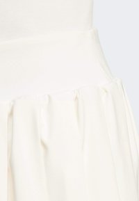 Jupe plissée blanche avec une taille lisse et texturée, mettant en avant un tissu léger et un drapé doux pour une silhouette fluide.