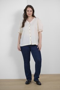 Chemisier crème à col en V, manches courtes bouffantes et ourlet droit. Associé à un jean en denim bleu foncé et des mocassins noirs.