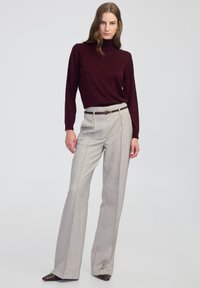 Burgundowa sweter z golfem zestawiony z jasnoszarymi, dopasowanymi spodniami z wysokim stanem z subtelnym kratkowanym wzorem oraz ciemnym akcentem paska.