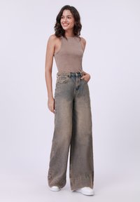 Beige ribbed tank top paired with wide-leg, faded denim jeans featuring a patterned belt, rounded hem, and worn texture. White sneakers complete the look.
