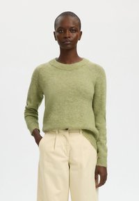 Hellgrüner Pullover mit rundem Ausschnitt und gerippten Bündchen, kombiniert mit cremefarbenen, plissierten Hosen. Weiche Textur, lässige Passform.