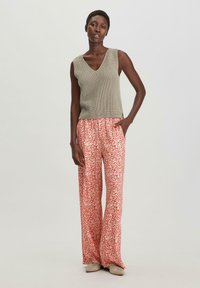 Lichtgewicht, olijfgroen, geribbeld gebreid mouwloos topje gecombineerd met vloeiende, hoogwaist rode bloemenprint broek. Geweven stof, losse pasvorm.