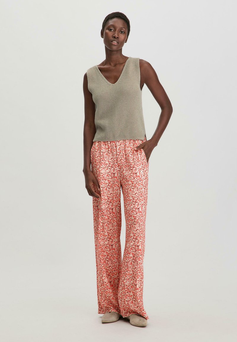 Lichtgewicht, olijfgroen, geribbeld gebreid mouwloos topje gecombineerd met vloeiende, hoogwaist rode bloemenprint broek. Geweven stof, losse pasvorm.