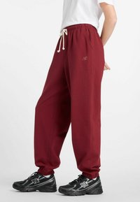 Bordeauxrode joggingbroek met elastische boorden en een tailleband met trekkoord. Machinegebreide stof met zijzakken; voorzien van een subtiel geborduurd logodetail.