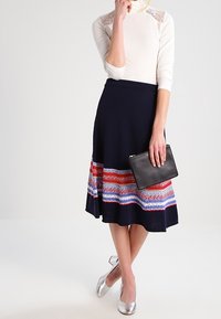 Laahus navy vaate neulottu hame, jossa on monivärinen kuvioitu helma. Yhdistetty tiukkaan valkoiseen pitsireunaiseen toppiin ja mustaan clutch-laukkuun. Hopeiset ballerinat viimeistelevät asun.