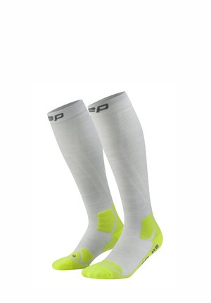 Weiße kniehohe Kompressionsstrümpfe mit neon-gelben Fersen- und Zehenbereichen, mit einem grauen Logo nahe dem oberen Bündchen.