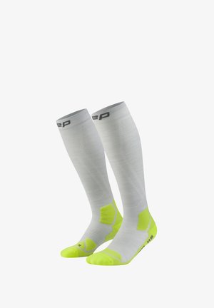 White knee-high compression socks with neon yellow heel and toe areas, featuring a gray logo near the top cuff.
