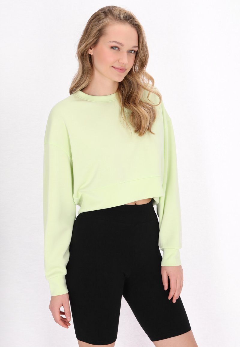 Felpa corta verde chiaro con maniche lunghe abbinata a pantaloni shorts neri. Texture morbida, design casual e vestibilità comoda.