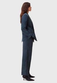 Completo su misura di colore blu navy con un elegante blazer e pantaloni a gamba larga. Texture liscia, design minimalista, abbinato a tacchi neri a punta.