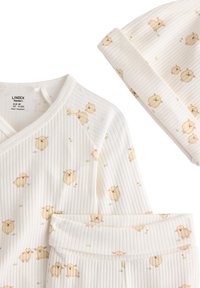 Hvid, ribbet nyfødtsæt med en omslagsbluse og bukser. Indeholder et fåremønster i beige, med en matchende hue, blødt stof og mild tekstur.
