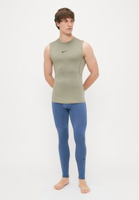 Ελαιόχρωμο αμάνικο τοπ και μπλε κολάν, και τα δύο φτιαγμένα από ελαστικό ύφασμα; διαθέτει ένα μικρό μαύρο λογότυπο Nike στο στήθος και στο πόδι.