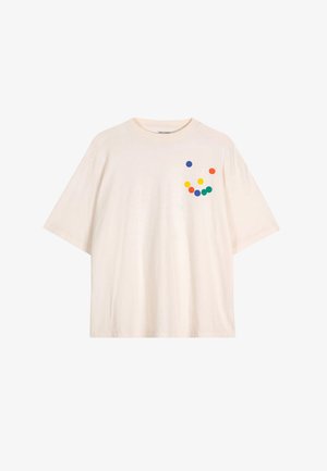 Krem majica oversized od pamuka s kratkim rukavima, koja ima šareni uzorak točkica u narančastoj, žutoj, zelenoj i plavoj boji.