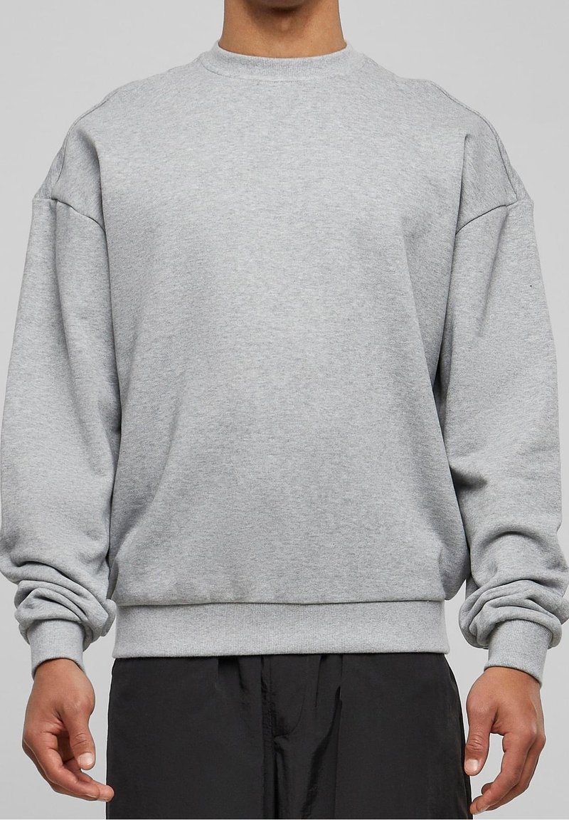 Sudadera de algodón gris con mangas largas, cuello redondo acanalado y puños. Presenta un diseño de hombros caídos y un corte relajado.