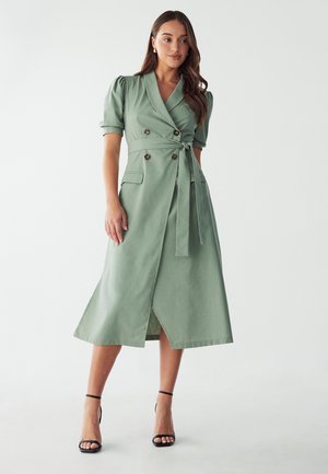 Green wrap dress with short puff sleeves, double-breasted buttons, self-tie belt, and a knee-length hem. Smooth texture with side slits.