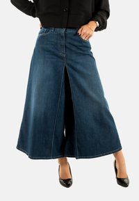 Culottes de mezclilla con cintura alta y abertura frontal, en azul oscuro. Cuenta con el clásico estilo de cinco bolsillos y costuras en contraste. Se llevan tacones negros.