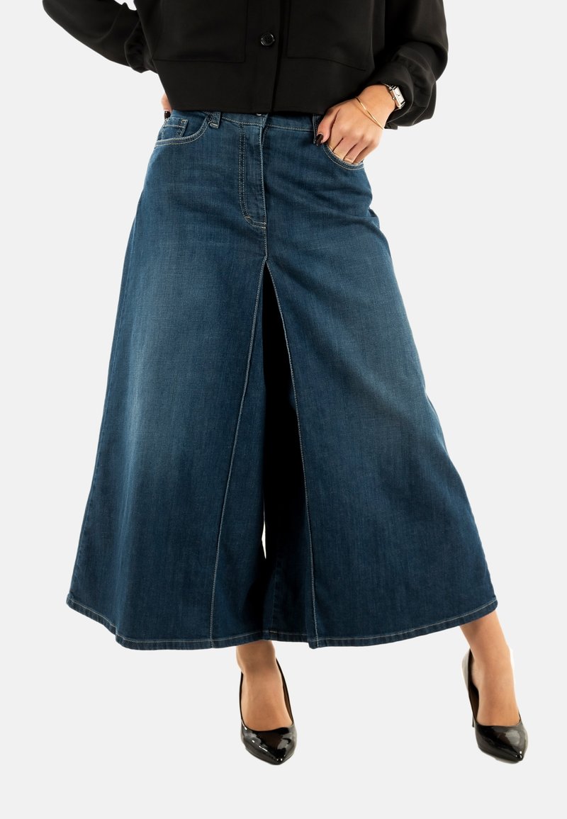 Culottes de mezclilla con cintura alta y abertura frontal, en azul oscuro. Cuenta con el clásico estilo de cinco bolsillos y costuras en contraste. Se llevan tacones negros.