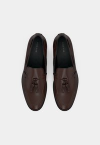 Mocassins en cuir marron avec détails découpés, accents à glands et finition lisse, dotés d'une semelle extérieure en caoutchouc noir et d'un intérieur rembourré.