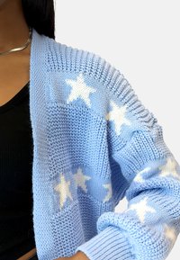 Cárdigan de punto azul claro con patrones de estrellas blancas, con puños acanalados y un diseño texturizado. Estilo de apertura frontal, tejido texturizado.