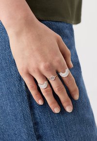Două inele pe o mână: unul cu un design semicircular și accente de diamant, iar celălalt având o piatră centrală rotundă și pietre mai mici.