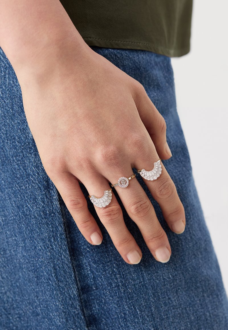 Două inele pe o mână: unul cu un design semicircular și accente de diamant, iar celălalt având o piatră centrală rotundă și pietre mai mici.