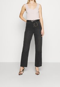 Czarne jeansy z wysokim stanem i prostymi nogawkami, z złotym okrągłym paskiem sprzączką. Górna część to jasnoróżowy, prążkowany top z dekoltem w kształcie litery V.