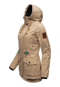 Veste imperméable beige avec une capuche doublée, des cordons de serrage et des accessoires décoratifs. Comprend deux poches avant et des détails contrastés sur les boutons.