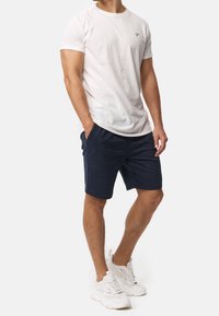 T-shirt blanc à manches courtes, shorts bleu marine et baskets blanches. Coton doux avec un col rond, les shorts disposent de poches latérales et d'une coupe décontractée.