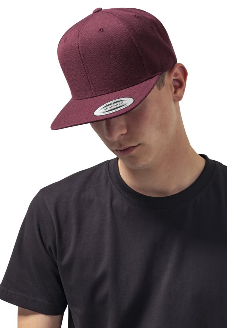 Burgundy snapback sapka lapos karimával, strukturált hatpaneles kialakítással és állítható pánttal egy fekete pólót viselő személyen.