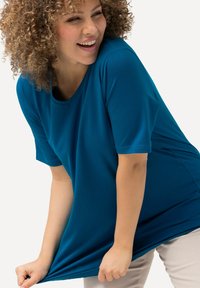 Tunic corto a maniche corte color teal con scollatura rotonda, realizzato in un tessuto liscio, caratterizzato da una vestibilità ampia e da un delicato drappeggio all'orlo.
