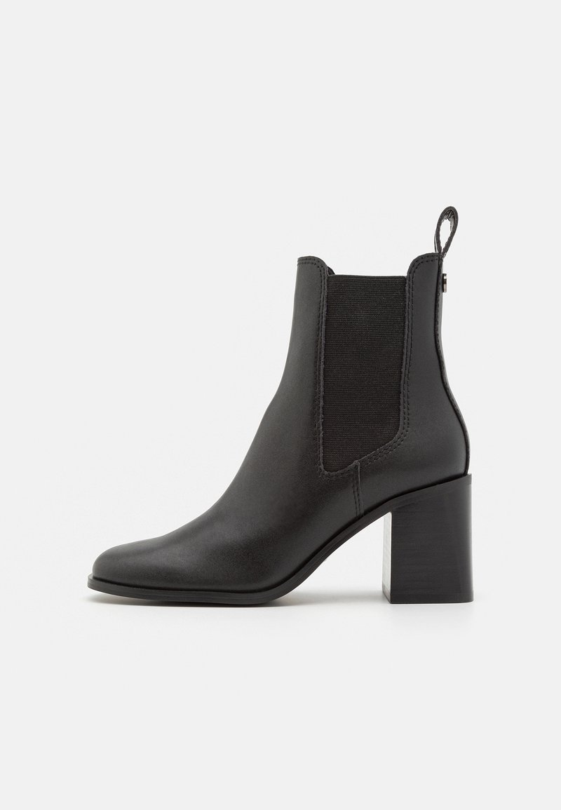 Bottine en cuir noir avec panneau latéral élastique, languette de traction et talon bloc sur fond blanc.