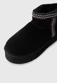 Sorte semsket ankelstøvletter med plussfôr og dekorativ beige søm langs toppen og sidekantene.