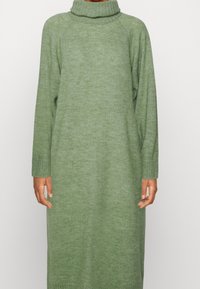 Langes, locker sitzendes, grünes Strickkleid mit Rollkragen, gerippten Manschetten und einer weichen Textur, das bis zur Mitte der Waden reicht.