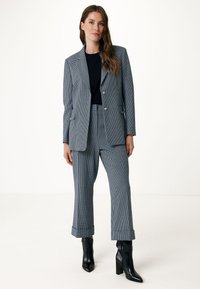 Grårutig kavaj med matchande vida byxor, med en skräddarsydd passform. Svarta anklarstövlar fulländar outfiten.